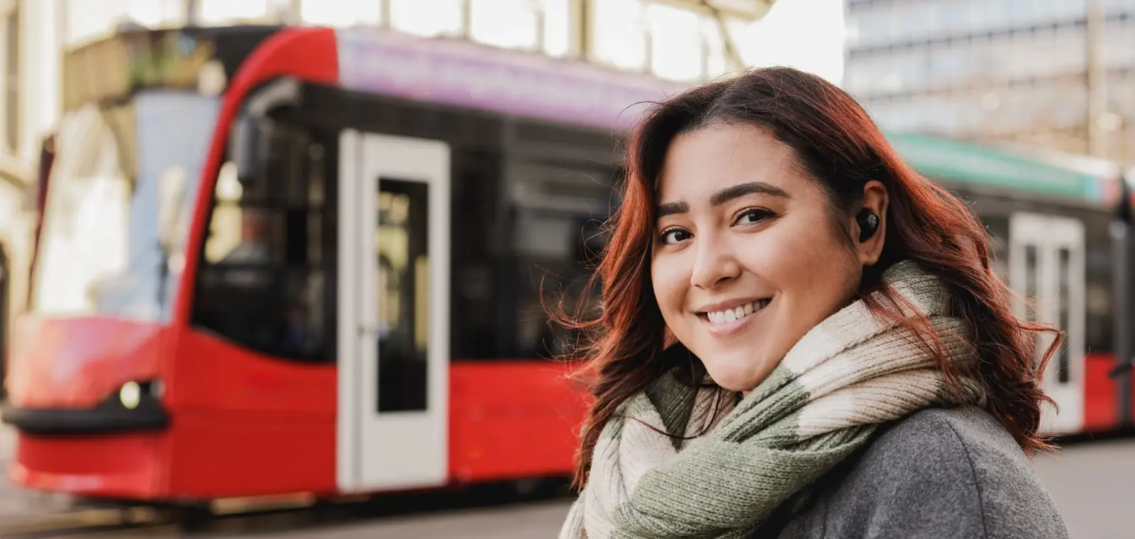 Lächelnde Fahrgästin mit Schal an einer Straßenbahnhaltestelle