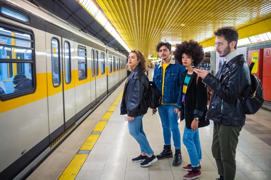 Vier junge Fahrgäste warten auf dem Bahnsteig einer U-Bahn-Station auf die Einfahrt des Zuges